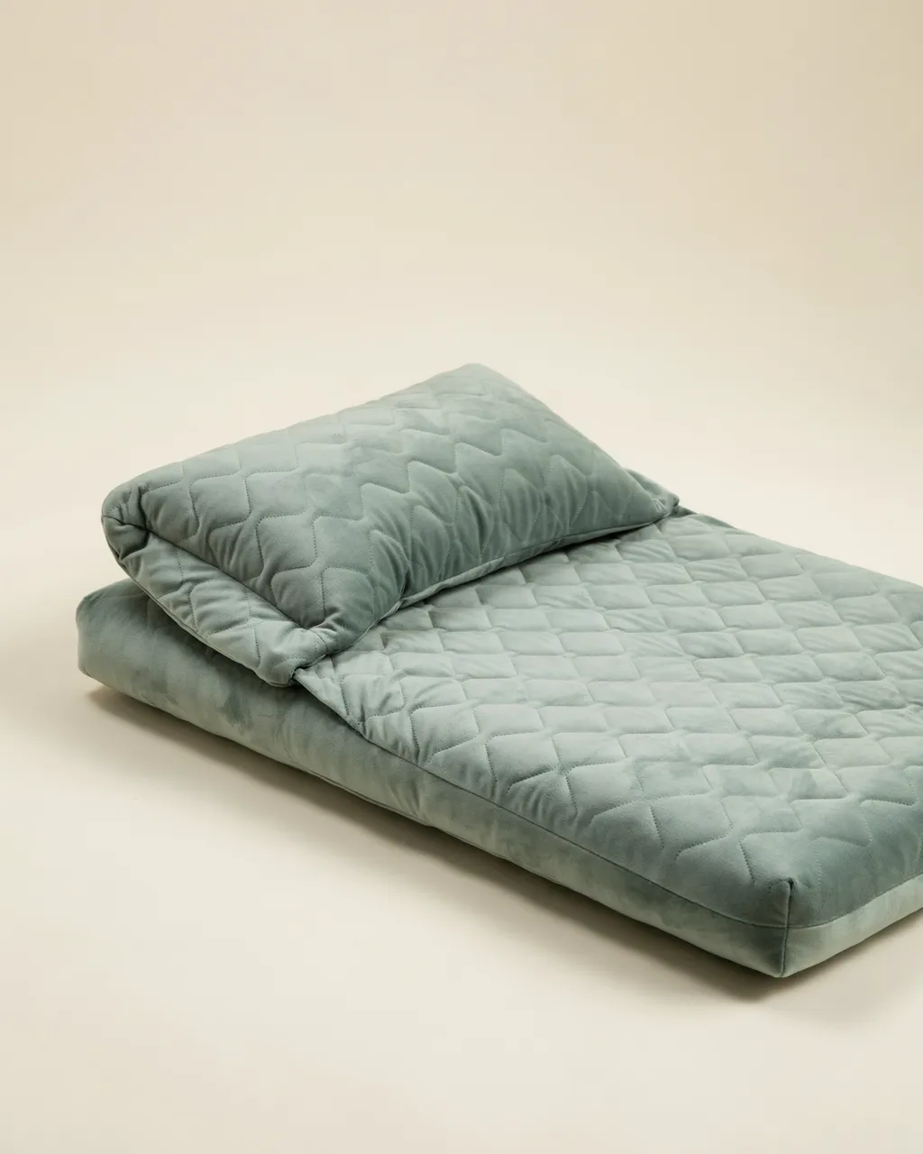 Gros plan sur le matelas vert sauge en velours matelassé et son coussin amovible posé à une extrémité